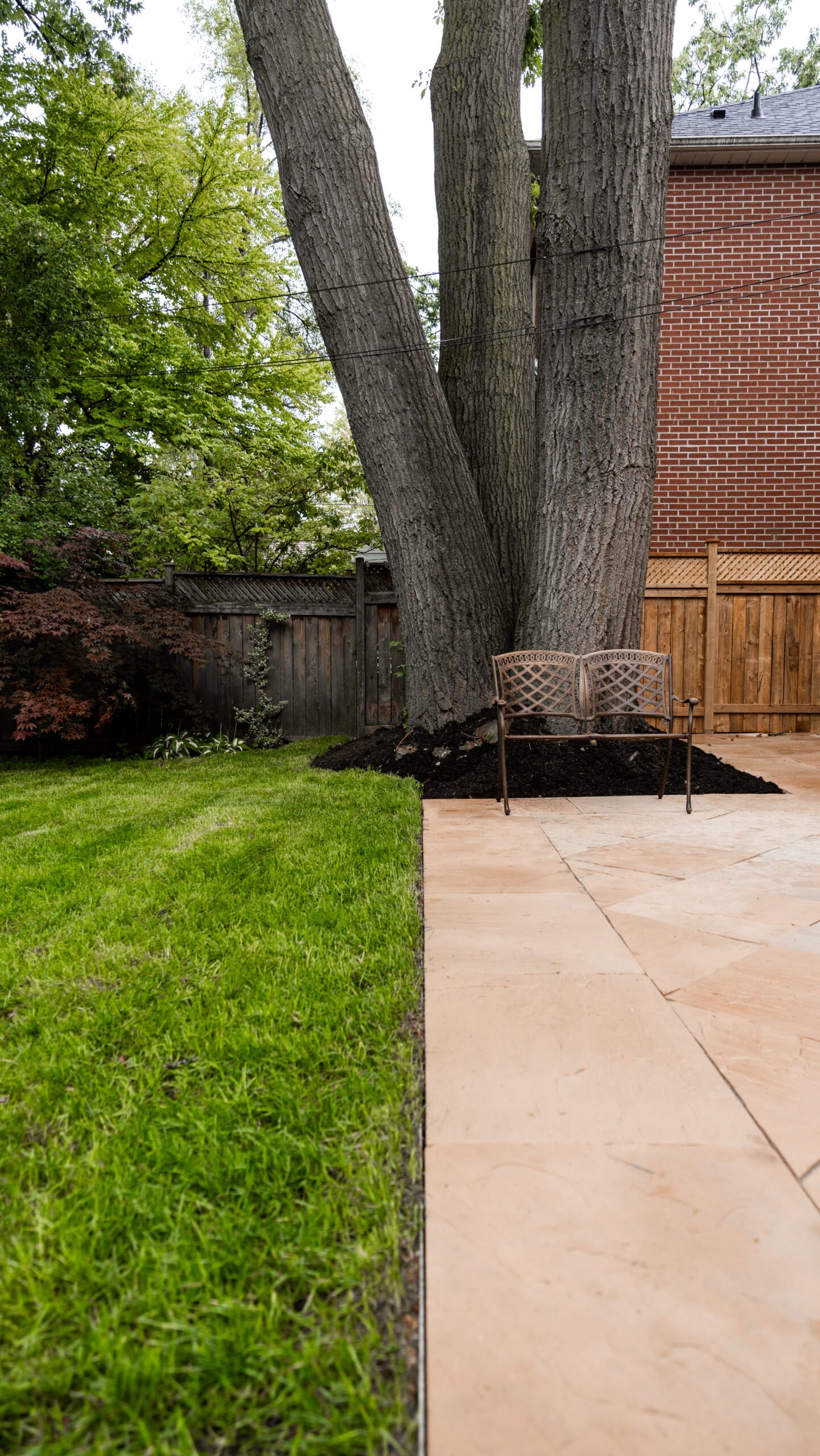 A luxury backyard featuring a mix of artificial turf, stone walkways, and custom garden beds by UBL Group.